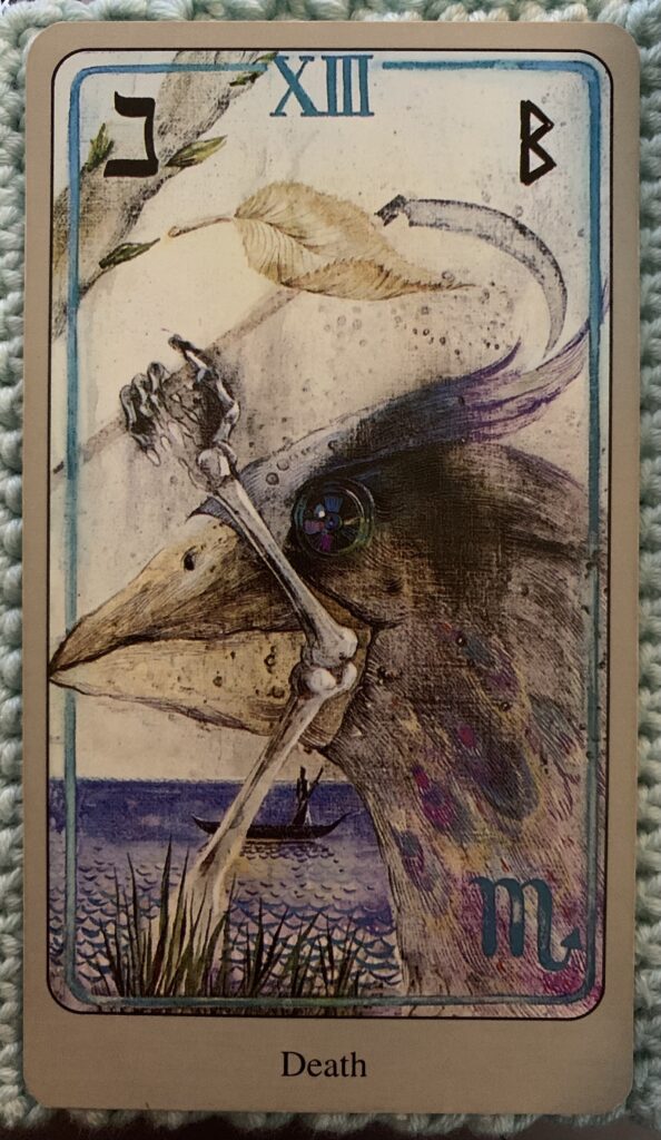 The Death card from the Haindl Tarot showing a peacock's head, a skeleton arm and hand holding a scythe. A boat with a ferryman appears in the water in the background. The glyphs for the Hebrew letter Nun, or fish, appears in the upper left-hand corner, while Beorc (Berkano, Birch Goddess) appears in the upper right. In the lower right hand corner is the astrological glyph for Scorpio. 